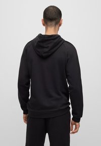 Svart hettegenser med snorhette, raglanermer, myk tekstur, og ribbede mansjetter og nederkant. Minimalistisk design uten synlige logoer.