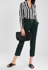 Blouse à rayures noires et blanches, pantalon vert sur mesure avec ceinture, sac à main en cuir noir, et sandales plates noires.
