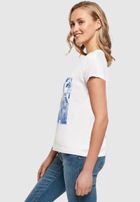 Hvid t-shirt med korte ærmer og blå grafisk print. Enkel design med afslappet pasform, lavet af blødt bomuldsstof.