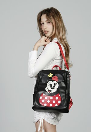 Mochila de imitación de cuero negra con detalles rojos, que presenta un gran gráfico de Minnie Mouse con lunares y un detalle de flor.