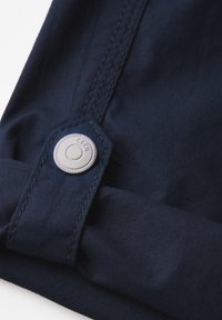 Navy stof met een zachte textuur, voorzien van een zilveren drukknoop en omgeslagen manchetdetails. Zichtbare stiksels accentueren het ontwerp.