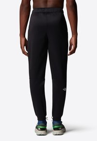 Black athletic pants made of stretch fabric, featuring an elastic waistband, tapered legs, and a logo on the right side.