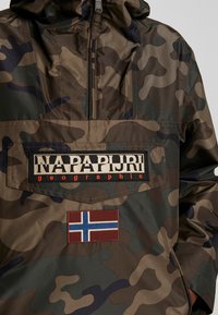 Kurtka w wzór kamuflażu w odcieniach brązu, zieleni i czerni, z dużą kieszenią z przodu, naszywką z logo oraz emblematem flagi norweskiej.