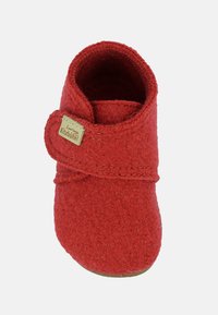 Czerwony filcowy kapcie o zaokrąglonym kształcie, z materiałowym paskiem i przeszyciami. Posiadają teksturowaną powierzchnię i małą metkę z logo.