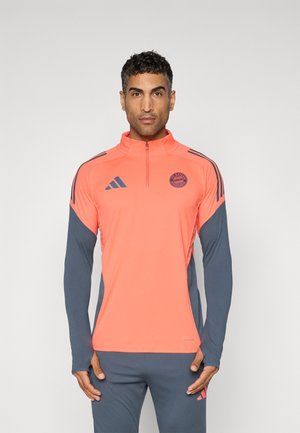Felpa sportiva zip-up rosso-arancio con maniche lunghe e pannelli laterali grigi; presenta il logo Adidas e un emblema rotondo della squadra sul petto.