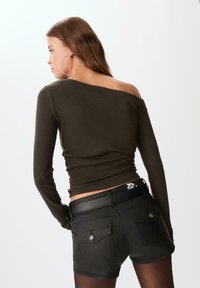 Mørkeoliven ribbet langærmet top med en asymmetrisk halsudskæring, parret med sorte denimshorts med baglommer og et logo på taljen.