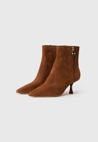 Botas de tobillo de ante marrón con punta afilada, tacón delgado y cremallera lateral con un acento decorativo en el herraje. Textura suave.