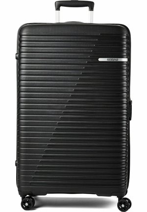 Schwarzer Hartschalenkoffer mit horizontalen Rillen, vier Spinner-Rollen, Teleskopgriff und American Tourister-Logo vorne.