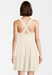 Crème-kleurige jurk met een aansluitend lijfje en een uitlopende rok. Bevat kruislings gesneden banden en een subtiele textuur. Geen zichtbare patronen of accenten.