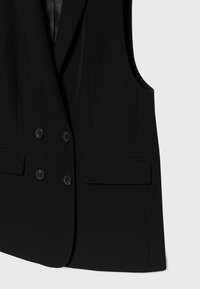 Blazer noir sans manches à double boutonnage avec deux paires de boutons et deux poches à rabat sur un fond clair uni.