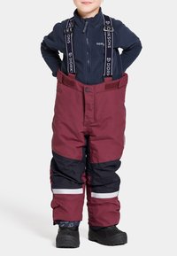 Vinröda och marinblå snökalsonger med justerbara remmar, hög midja och reflexdetaljer. Bärs över en marinblå fleecejacka med dragkedja och svarta stövlar.