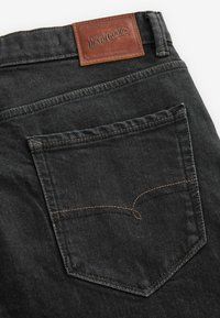 Mustat farkut, joissa on nahkainen תagin "Premium Denim Goods" ja takatasku, jossa on tonalisointi.