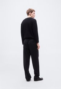 Μαύρο πλεκτό πουλόβερ με ριχτούς ώμους, σε συνδυασμό με μαύρο παντελόνι χαλαρής εφαρμογής με ελαστική μέση. Λεπτή υφή και μινιμαλιστικός σχεδιασμός.