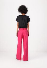 Zwarte top met korte mouwen en felroze hoge taille wijde broek. De achterkant van de top heeft een klein ritsdetail. Glad stof.