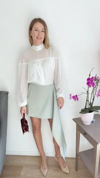 Blusa branca e transparente com decote em babados e mangas longas; saia assimétrica verde menta; sapatos nude; bolsa bordô; orquídea em vaso próxima.