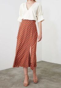 Gonna midi marrone a pois con uno spacco laterale, realizzata in un tessuto leggero. Abbinata a una blusa bianca a maniche corte e sandali con cinturino.