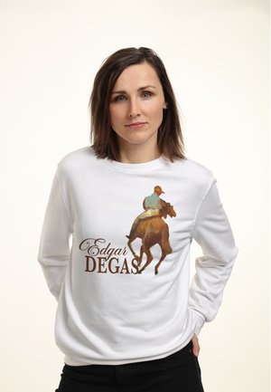Femme aux cheveux bruns mi-longs portant un sweat-shirt blanc avec un cavalier sur un cheval et le texte "Edgar Degas".