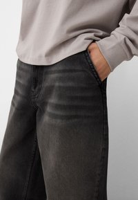 Tummanharmaat farkut suoralla leikkauksella ja hienovaraisilla haalistumisdetaileilla. Yhdistetty vaaleanharmaan pitkähihnaisen paidan kanssa. Pehmeä kangasrunko.