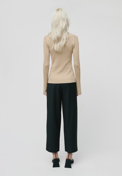 Top beige a maniche lunghe e coste abbinato a pantaloni neri a gamba larga a vita alta. Caratterizzato da un design minimale e sandali neri con tacco a blocco eleganti.