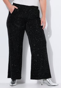Pantaloni neri a gamba larga in tessuto testurizzato e scintillante, con una finitura luccicante e tasche laterali, abbinati a stivaletti argentati.