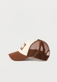 Καφέ και μπεζ καπέλο τύπου trucker με πλέγμα στο πίσω μέρος και λογότυπο σε ένθετο στο επάνω μέρος, εμφανίζεται σε απλό ανοιχτόχρωμο φόντο.