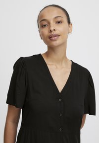 Vestido negro con mangas cortas abombadas, escote en V y botones en la parte delantera. Diseño sencillo y textura suave.