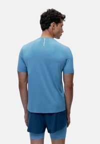 Šviesiai mėlyna sportinė marškinėliai trumpomis rankovėmis, lygi tekstūra ir atšvaitinė logotipo detalė nugaros pusėje. Tinkama su tamsiai mėlynomis šortais.