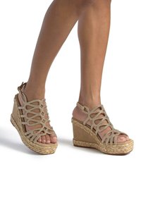 Sandali con zeppa beige, caratterizzati da una suola in corda intrecciata, cinturini intrecciati e dettagli in strass. Design con punta aperta e cinturino alla caviglia.