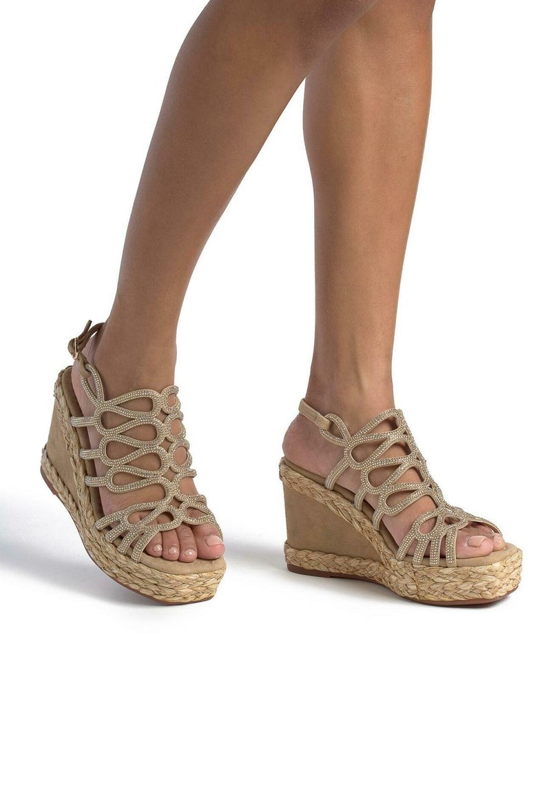 Sandali con zeppa beige, caratterizzati da una suola in corda intrecciata, cinturini intrecciati e dettagli in strass. Design con punta aperta e cinturino alla caviglia.