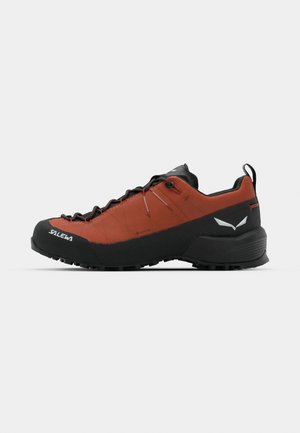 Red and black hiking shoe with a textured surface, rubber toe cap, durable lace system, and a rugged sole for traction.