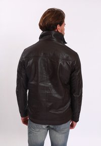 Brun läderjacka med hög krage, strukturerade axlar och slät baksida. Mjuk textur med sömdetaljer och figursydd design.