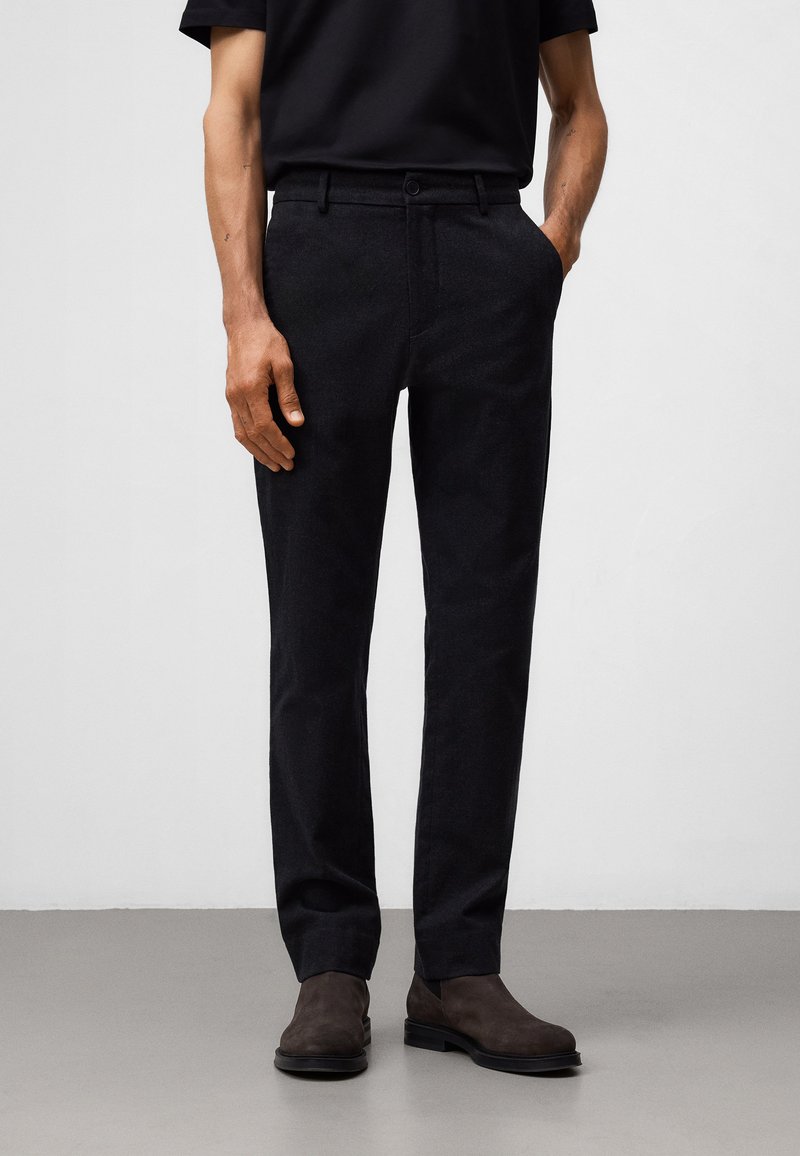 Ciemne, dopasowane spodnie wykonane z teksturowanej tkaniny, z prostym krojem, szlufkami na pasek i zapięciem na guzik, w połączeniu z brązowymi butami.