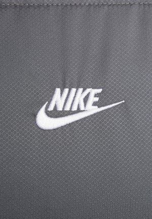 Tejido gris texturizado con un patrón hexagonal, que presenta un logo de Nike bordado en blanco en forma de swoosh.