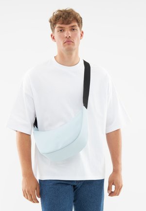 Lyseblå skuldertaske med en buet form, lavet af glat materiale, udstyret med en sort justerbar rem og diskret branding på forsiden.