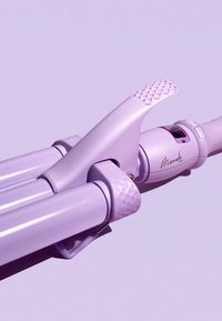 Fer à friser violet avec une prise texturée, des barils cylindriques lisses et un levier pour l'opération. Arbore un logo élégant sur le boîtier.