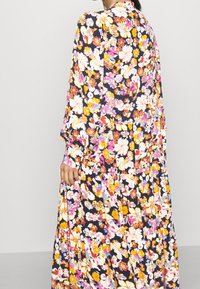 Robe maxi florale à manches longues, avec un fond bleu marine sombre orné de fleurs colorées dans des tons de rose, jaune et blanc.