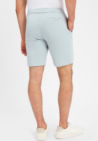 Lichtblauwe sportshorts van zachte stof met een elastische tailleband, voorzien van een achterzak en opgerolde zomen. Draagt bij witte sneakers.