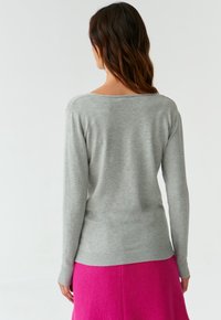 Grauer Langarmpullover mit weit ausgeschnittenem Ausschnitt und geripptem Saum, kombiniert mit einem fuchsiafarbenen Rock, der eine glatte Textur und eine taillierte Passform zeigt.