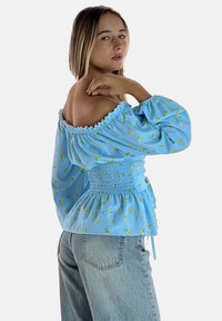 Blusa blu a spalle scoperte con motivo floreale, vita arricciata, maniche a sbuffo e orlo peplum, abbinata a jeans a vita alta blu chiaro.