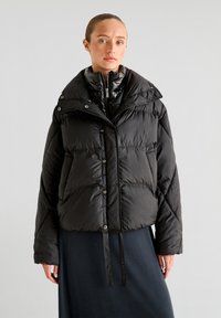 Sort polstret jakke med stort krave, trykknaplukning og en let cropped silhuet. Glat, blankt materiale med vandrette sømme.