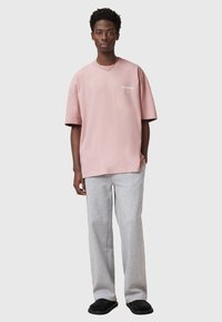 Camiseta de algodón rosa con mangas cortas y cuello redondo, combinada con pantalones de chándal grises, que cuentan con un corte relajado y bolsillos laterales.