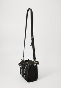 Black shoulder bag with a structured design, featuring white branding, gold hardware, and a detachable strap. Textured fabric and metallic accents.