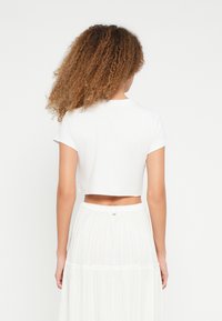 Witte cropped t-shirt met korte mouwen, zachte textuur en een ronde hals, gedragen met een witte plissérok die soepel valt.