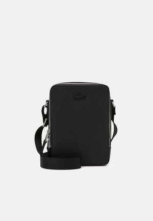 Sac bandoulière rectangulaire noir texturé avec fermeture éclair et sangle réglable sur fond uni.