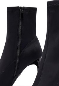 Botas negras hasta el tobillo con un acabado suave y mate, cierre lateral con cremallera y un elegante tacón de aguja brillante. Presentan detalles cosidos y un diseño ajustado.
