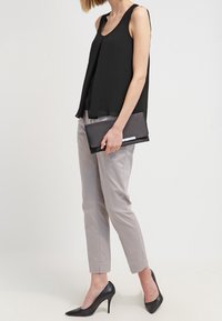 Černý top bez rukávů s volným střihem, spárovaný se světle šedými zúženými kalhotami a černými lodičkami s špičatou špičkou. Drží černou kabelku.