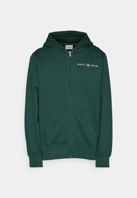 Sweat à capuche zippé vert en tissu doux. Comprend un logo sur la poitrine, des poches kangourou et une capuche avec cordon de serrage. Coupe classique.