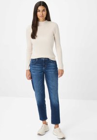 Maglietta a maniche lunghe ribbed color beige chiaro con un colletto alto, abbinata a jeans scuri a gamba affusolata e sneakers beige chiare.