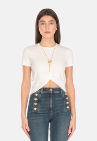 Top bianco a maniche corte con design frontale annodato. Abbinato a jeans in denim a vita alta con dettagli in bottone dorato.