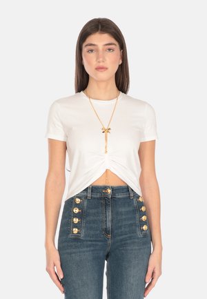 Top bianco a maniche corte con design frontale annodato. Abbinato a jeans in denim a vita alta con dettagli in bottone dorato.